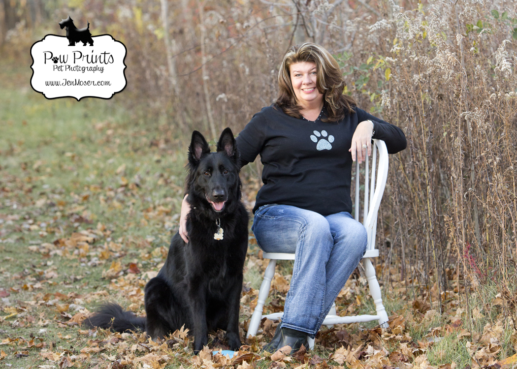 Indiana Pet Photographer Jen Moser of Paw Prints Pet Photography photographs a black german shepherd and his owner sitting on a chair at Matea Park in Fort Wayne, Indiana in the fall leaves